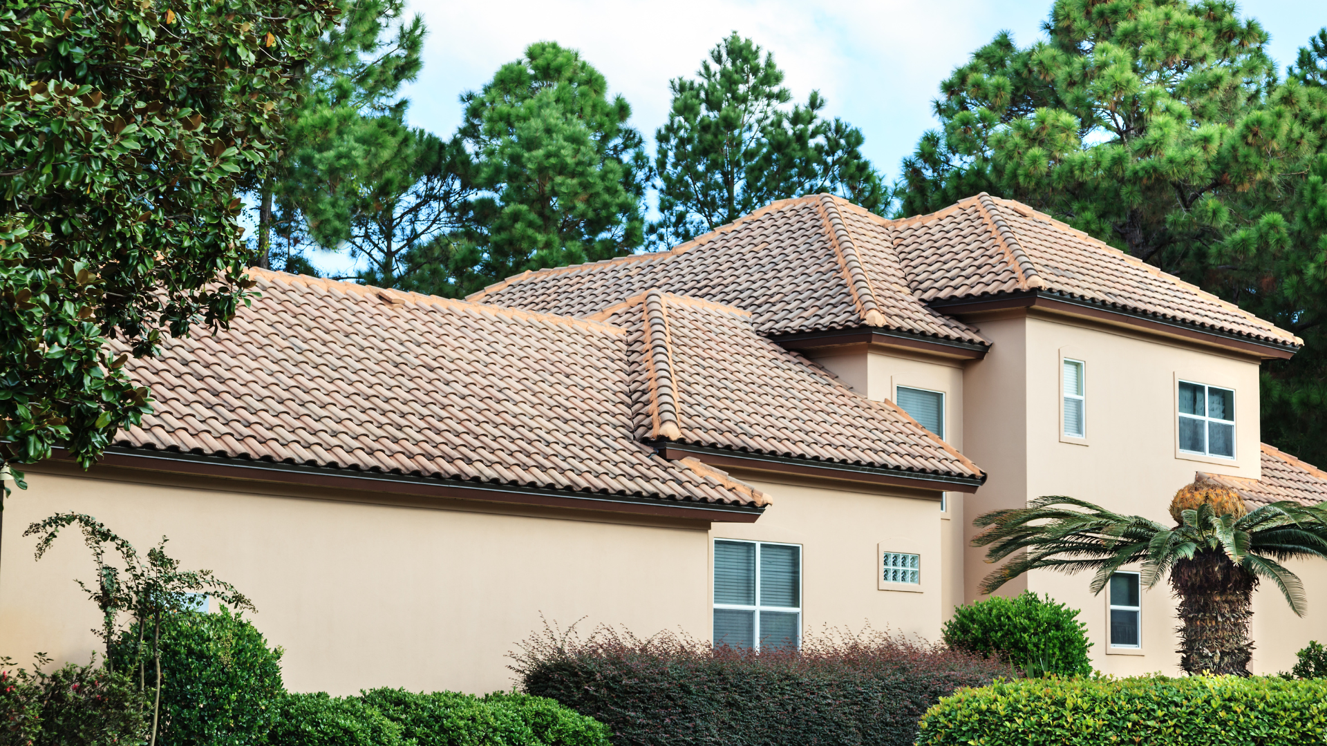 A large house with a tiled roof is surrounded by trees