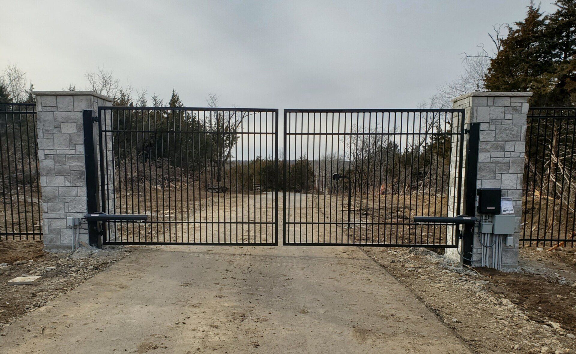 A metal gate is open on a gravel road.