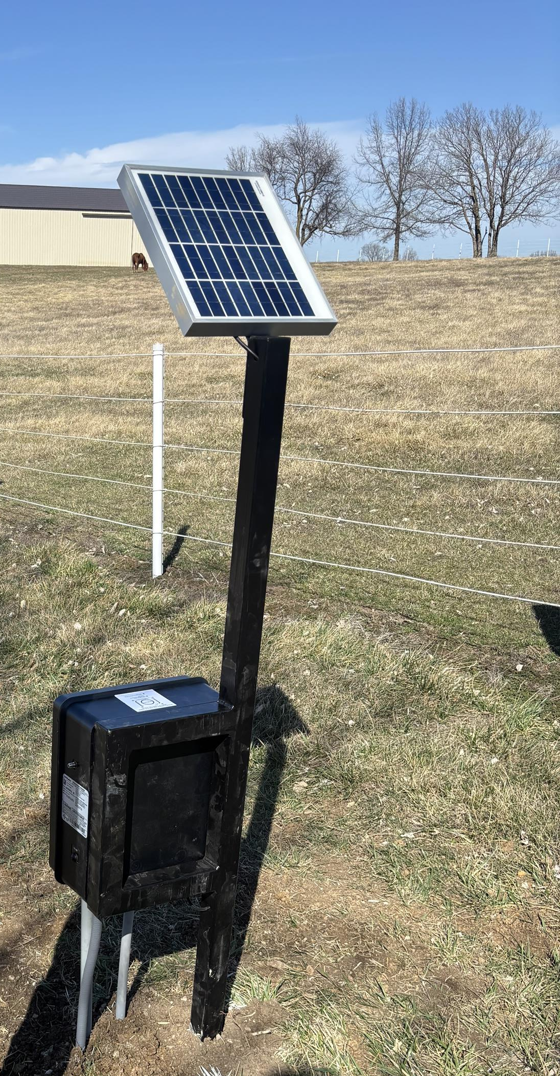 A solar panel is sitting on top of a pole in a field.
