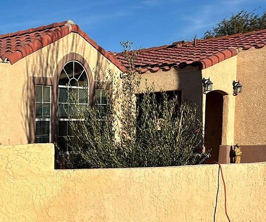 Spanish-style house with red tile roof, arched window, and yellow stucco wall under a blue sky