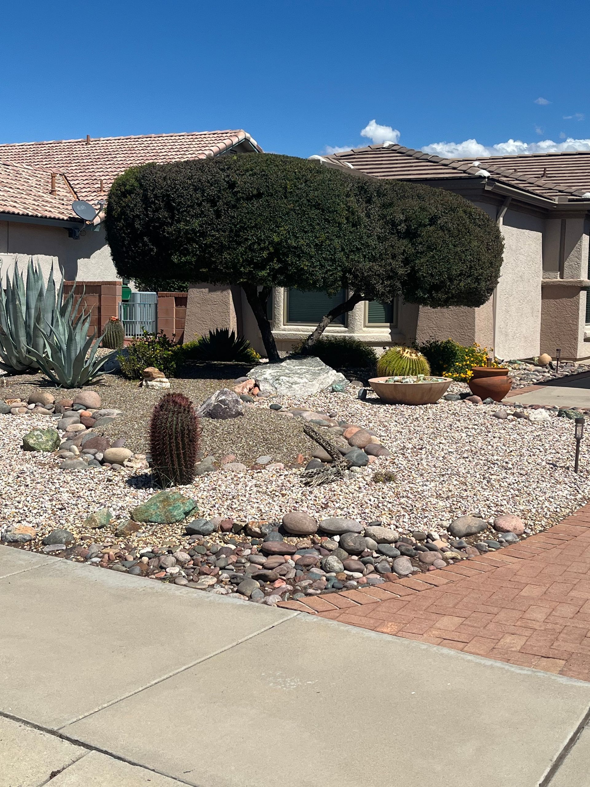 Desert-style house front with terra-cotta exterior, leafless trees, rocks, and a garage under cloudy skies