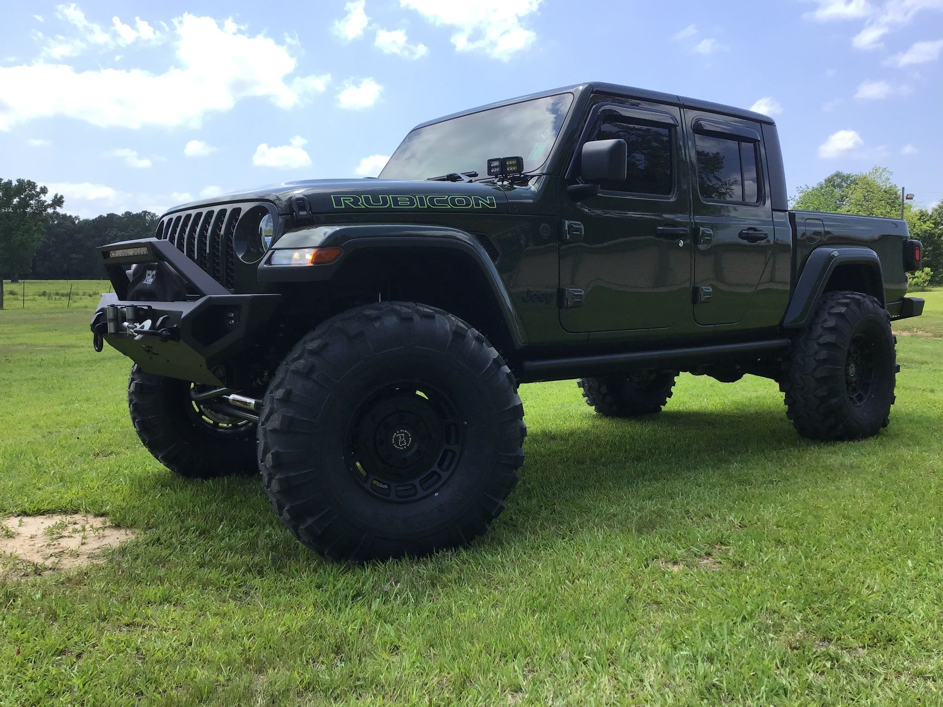 Black lifted Jeep Wrangler parked on grass under a partly cloudy sky