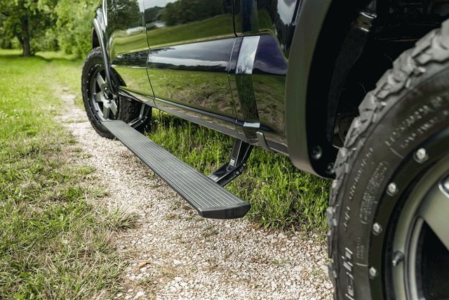 Black pickup truck with side step parked on gravel beside grass and trees