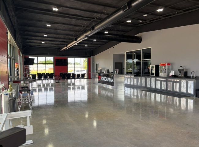 Empty modern showroom with polished concrete floor, black ceiling beams, and glass counters along the right side.