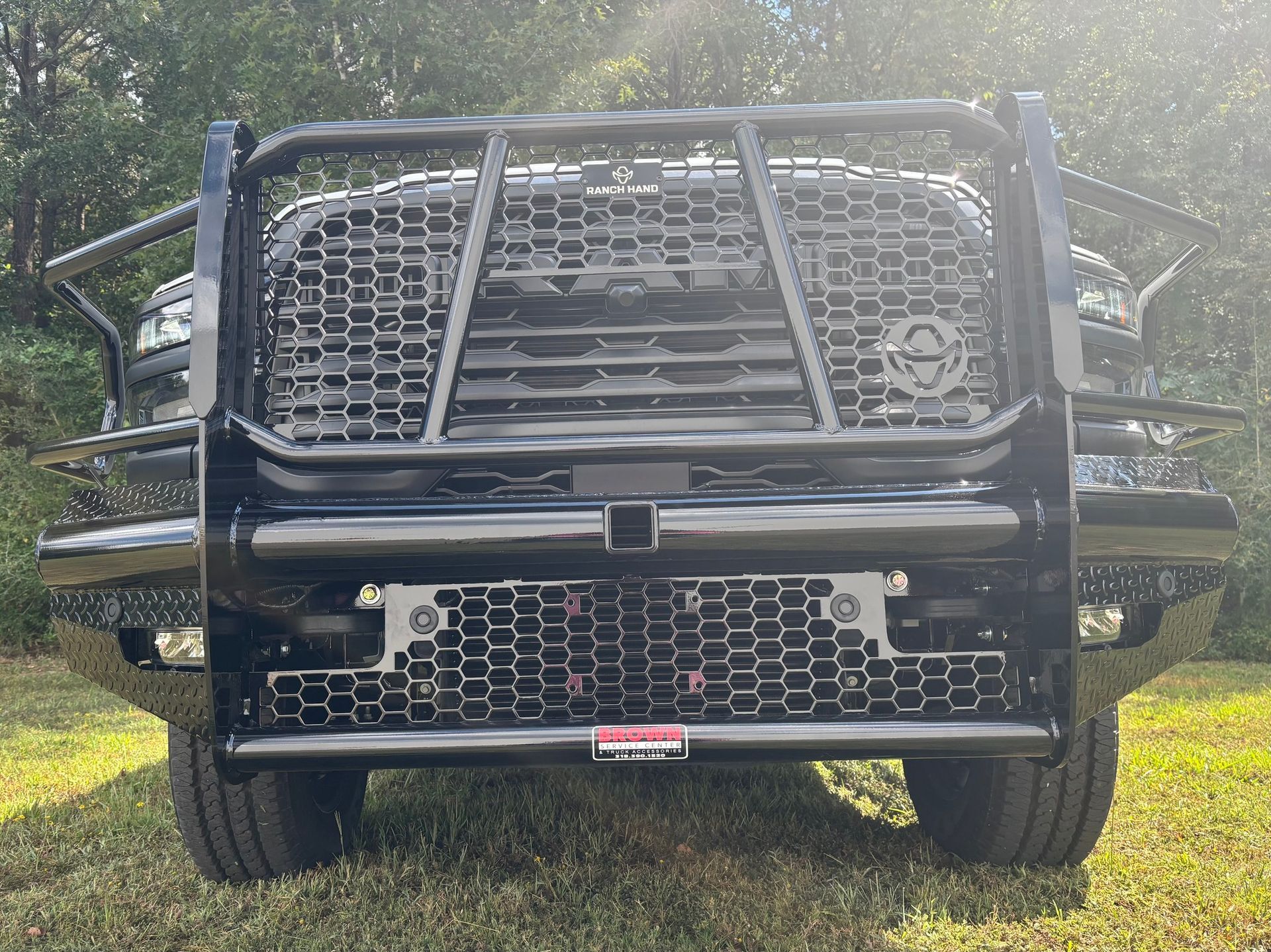 Front view of a black truck with a grille guard, parked on grass in bright sunlight