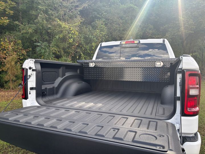 Open white pickup truck bed with tailgate down, parked outdoors in a wooded area