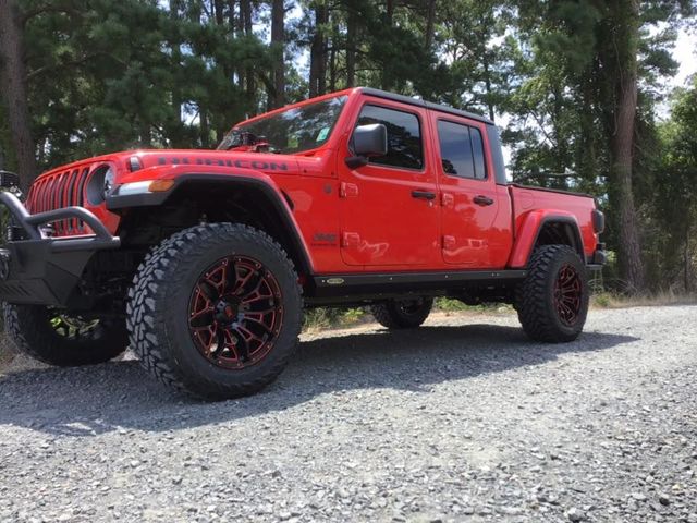 Red four-door Jeep pickup parked on gravel in a wooded area