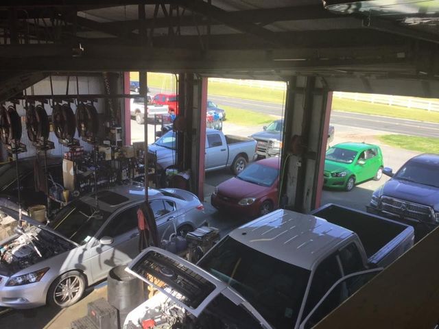 Auto repair shop with several cars parked inside, including a silver car and a green van by the open bay door
