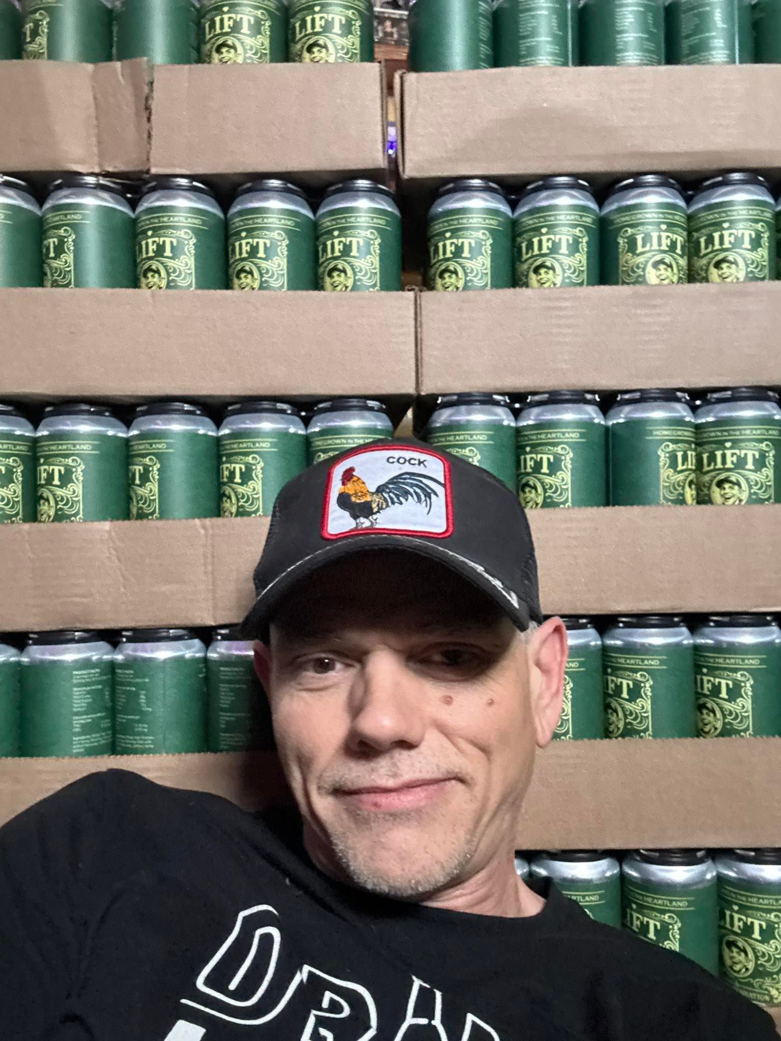 Man in black cap and shirt posing before stacked green cans on store shelves