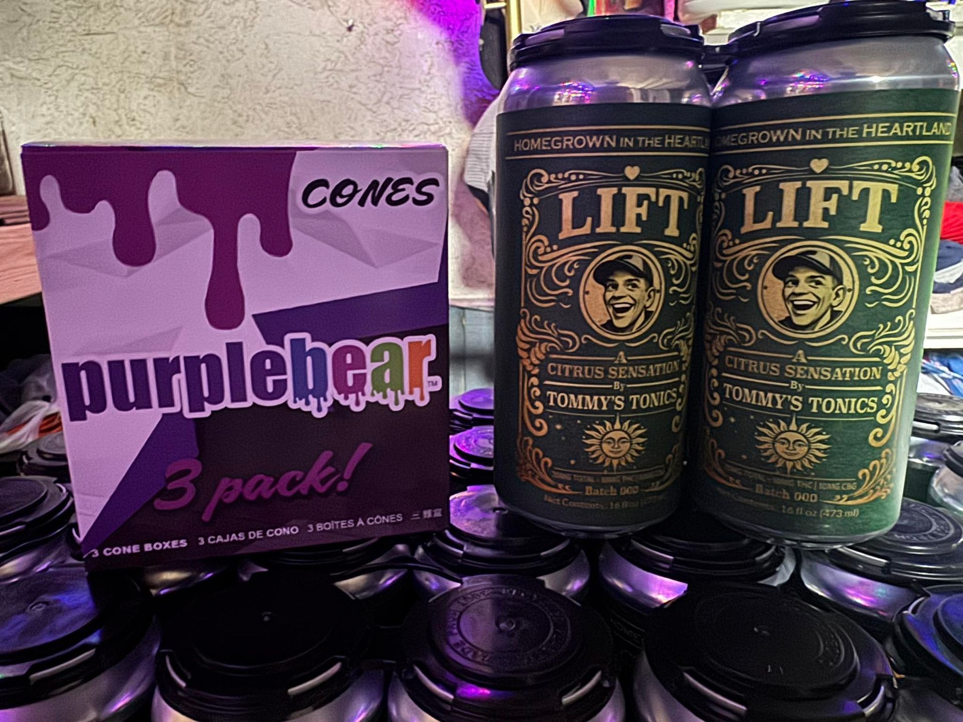 Purplebear snack bags beside two Lift tonic cans stacked on black containers.