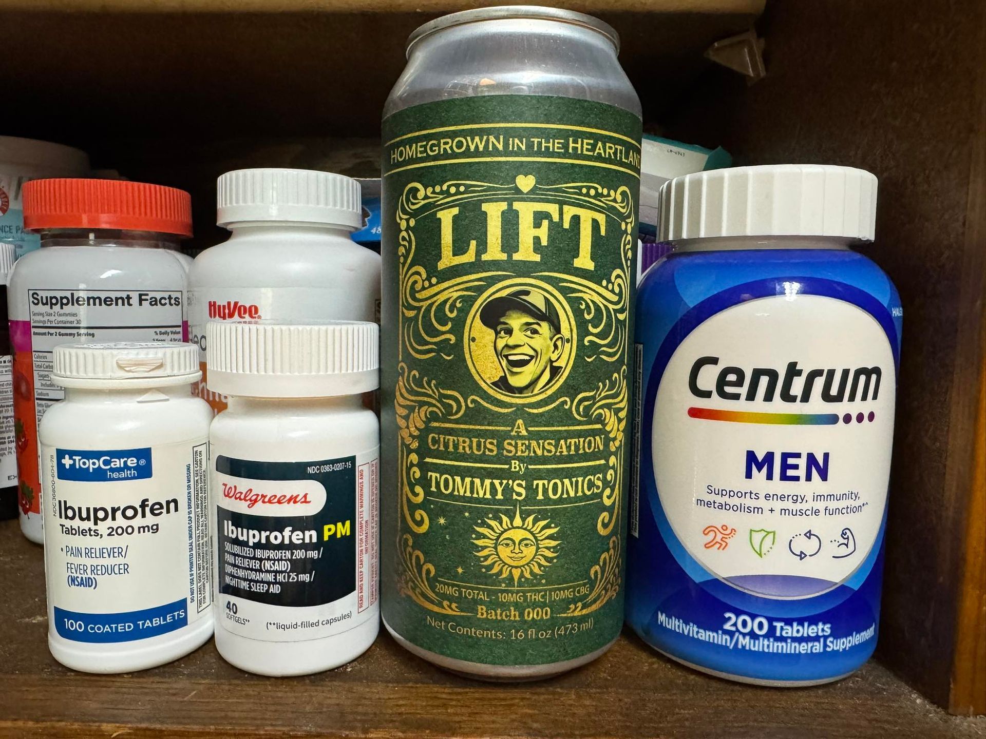 Assorted vitamins and medicines on a shelf, including a green LIFT can and a blue Centrum Men bottle.