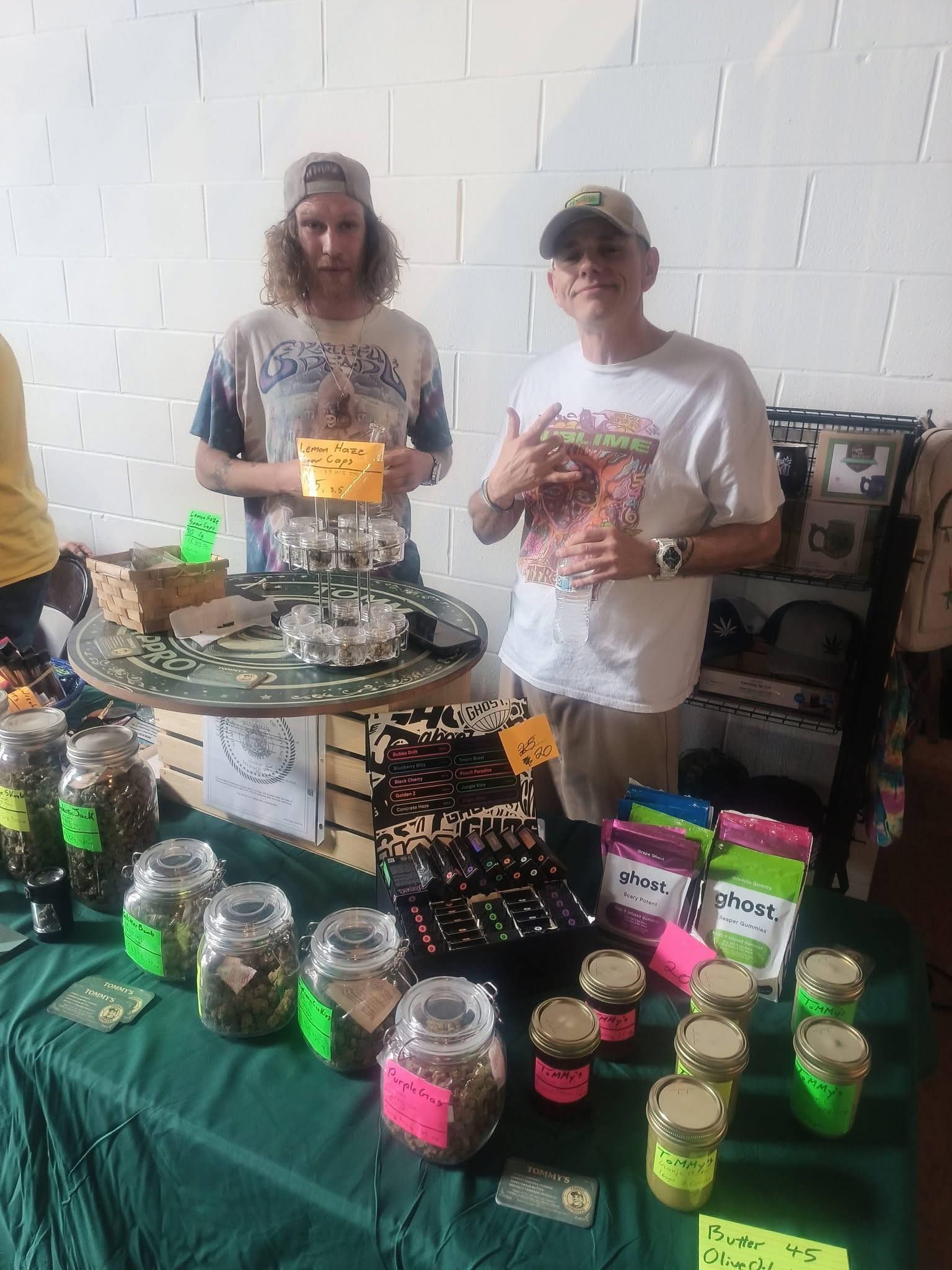 Two people at a vendor table displaying jars and packaged goods at a market booth.