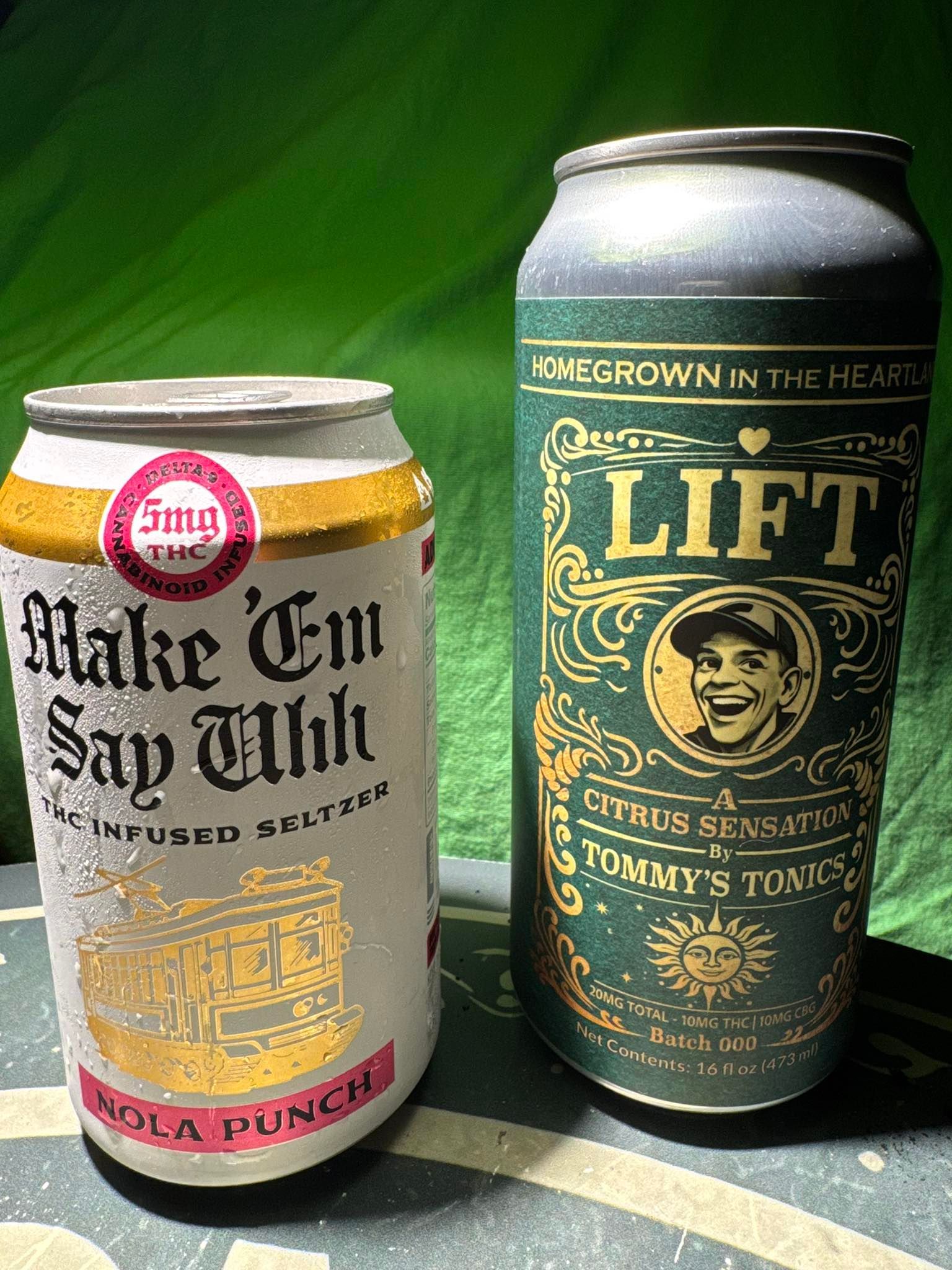 Two canned drinks on a green background: “Make ’Em Say Uncle” and a tall “LIFT” citrus soda can.