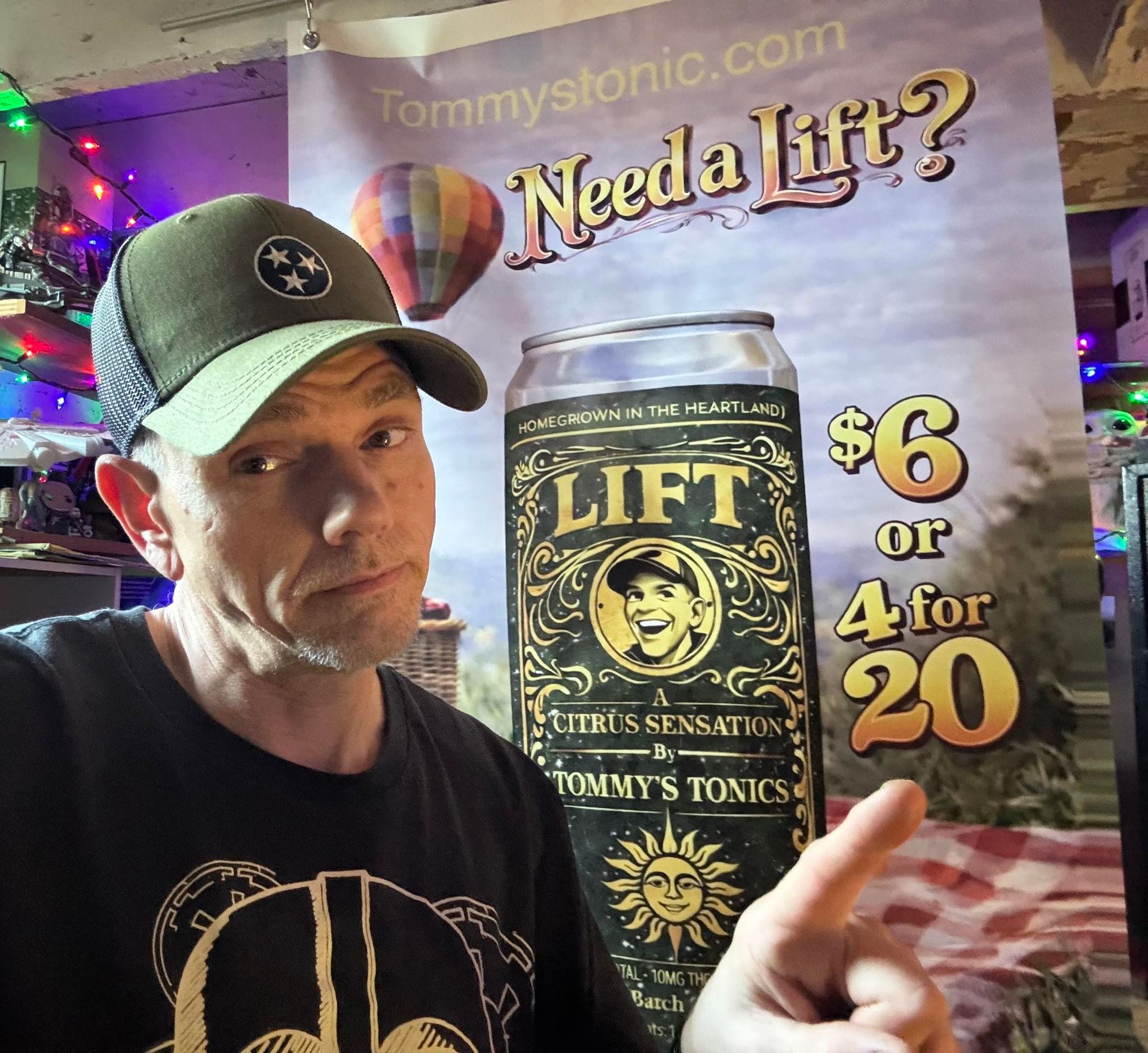 Man posing beside a “Need a Lift?” poster advertising Tommy’s Tonics LIFT, $6 or 4 for 20.