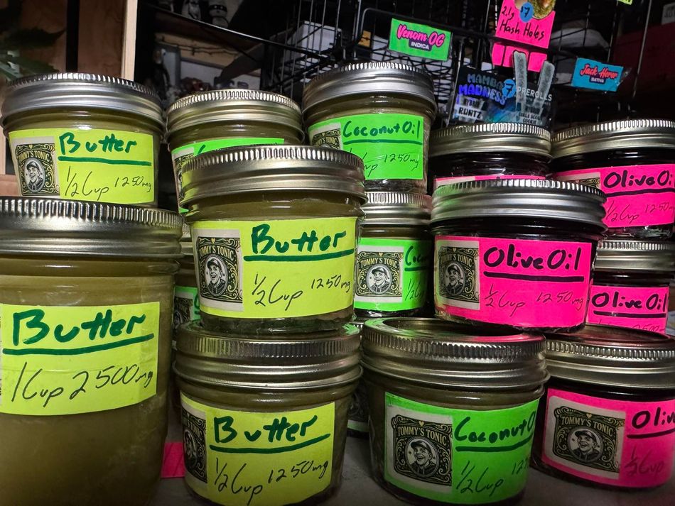 Jars of butter, coconut oil, and olive oil with colorful handwritten labels stacked on a market shelf