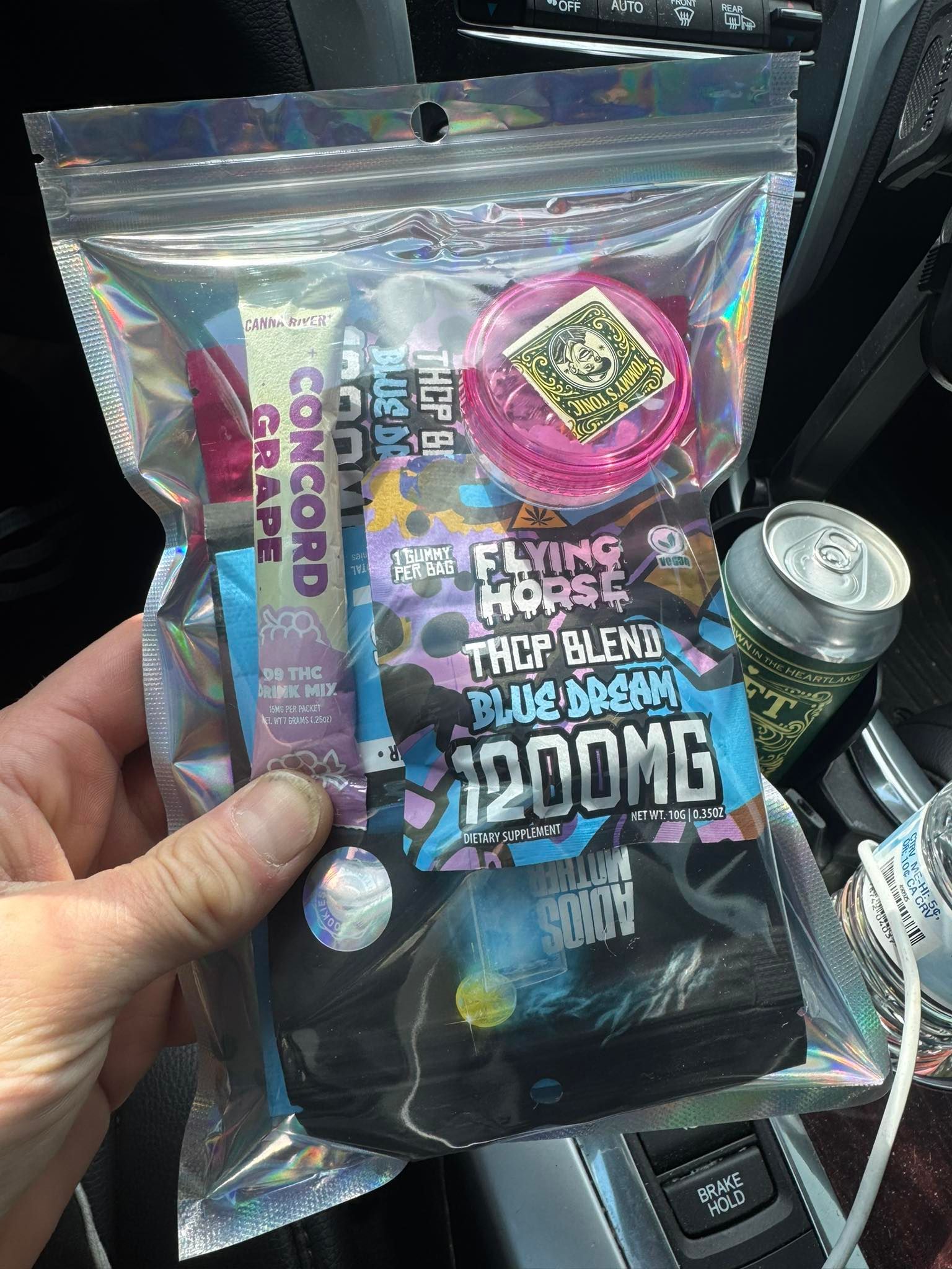 Hand holding a holographic pouch of candy with colorful text and a 200mg label in a car.
