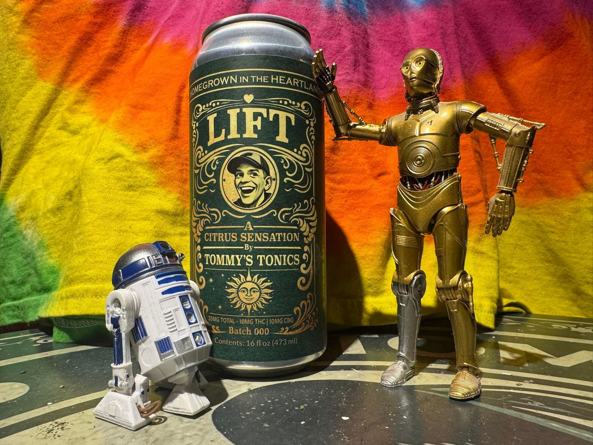 R2-D2 and C-3PO figurines beside a Lift soda can on a colorful tie-dye background