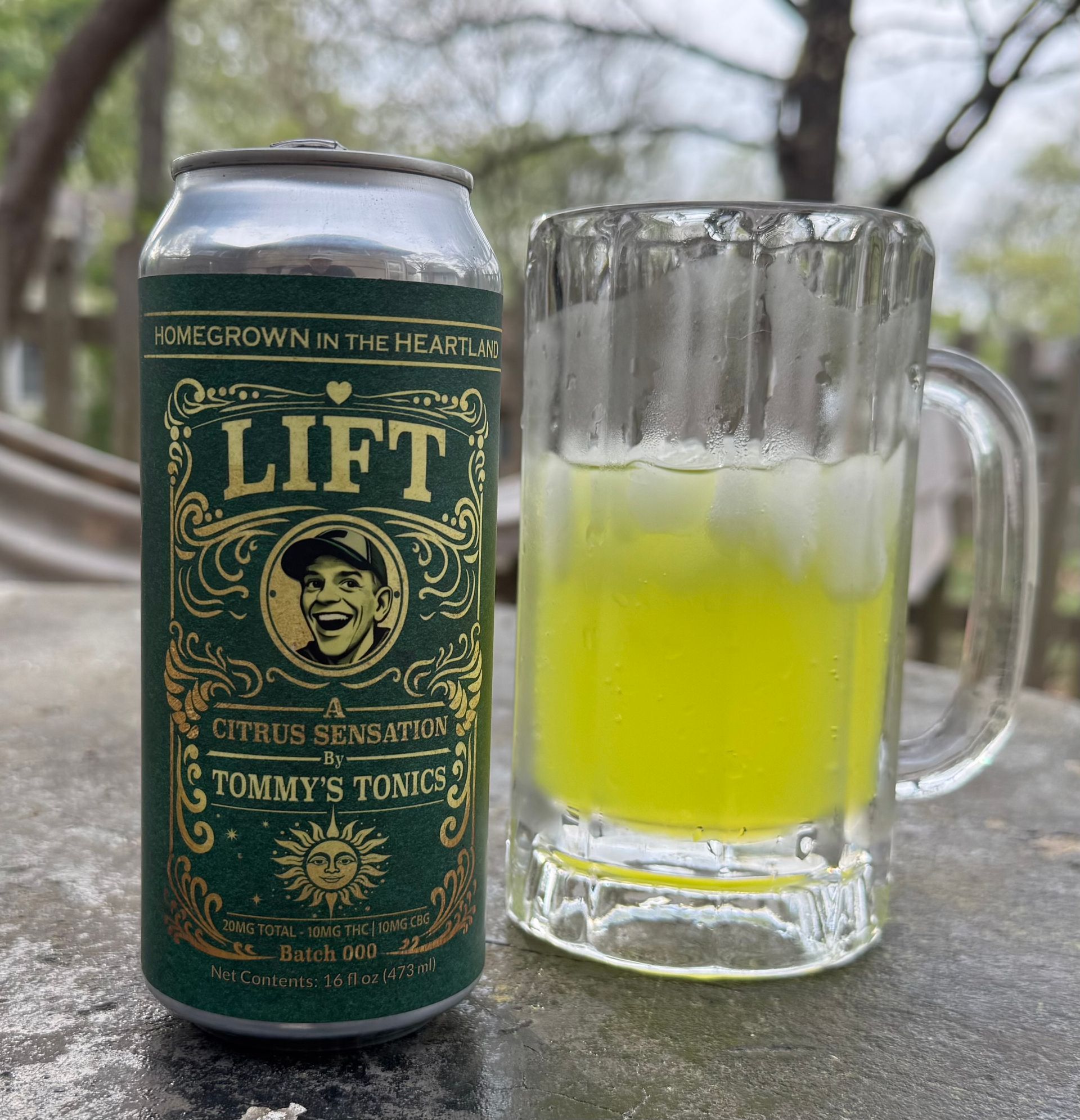 Green Lift citrus seltzer can beside a glass mug of neon yellow drink on a stone table outdoors