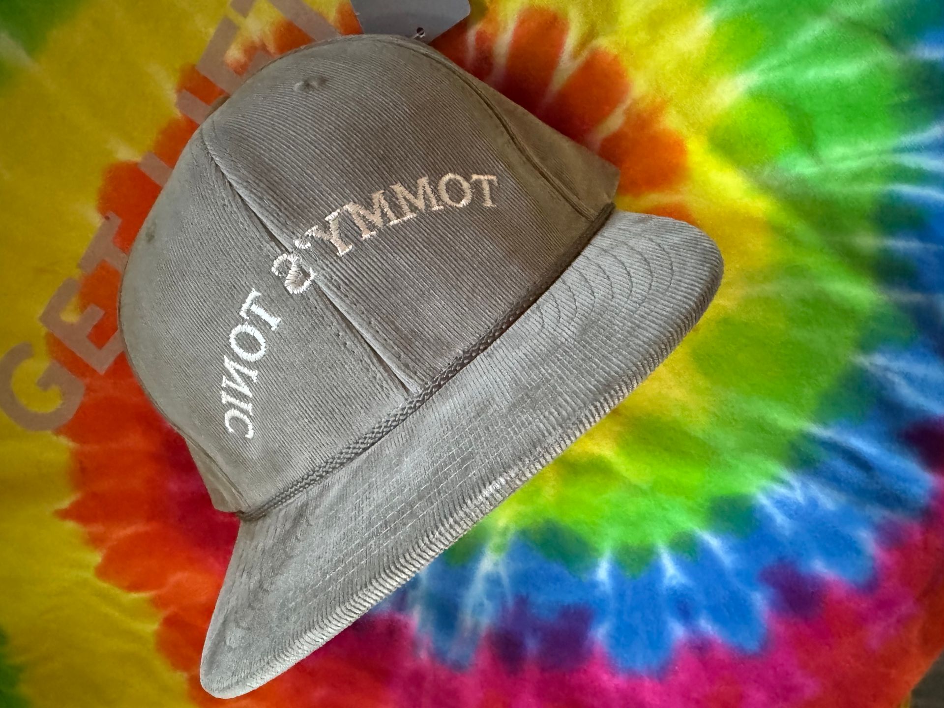 Gray cap with white text on a rainbow tie-dye background