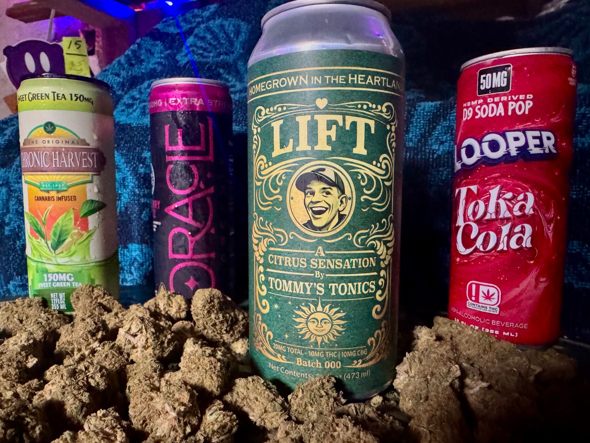 Four colorful soda cans standing in dirt, including Grace, Lift, and Dooper Tokai Cola bottles