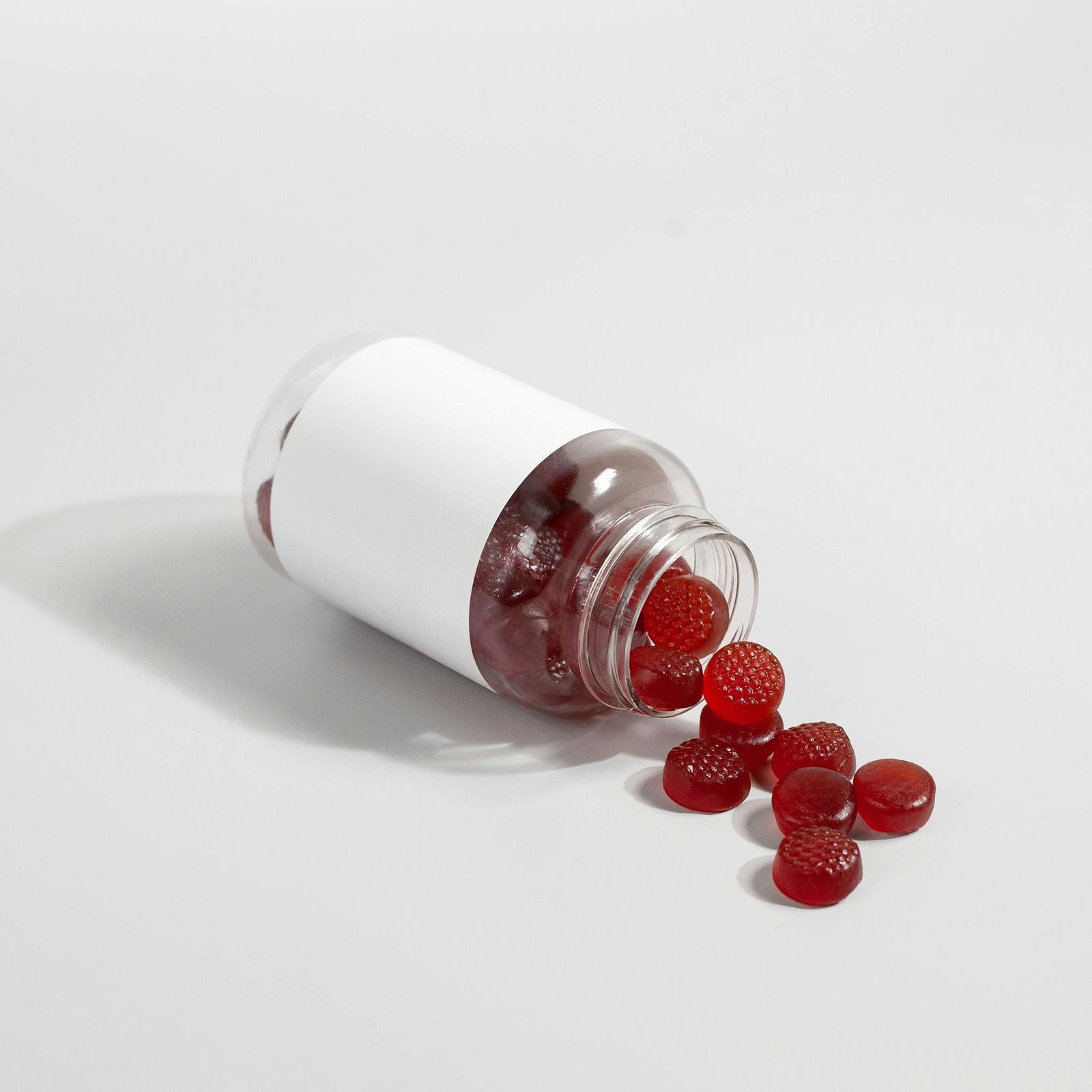 Spilled white pill bottle with red tablets scattered on a white surface