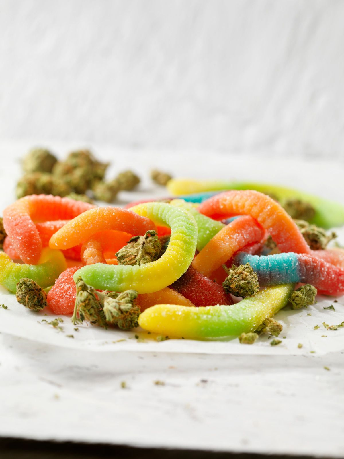 Colorful gummy worms on a white surface with scattered crumbs
