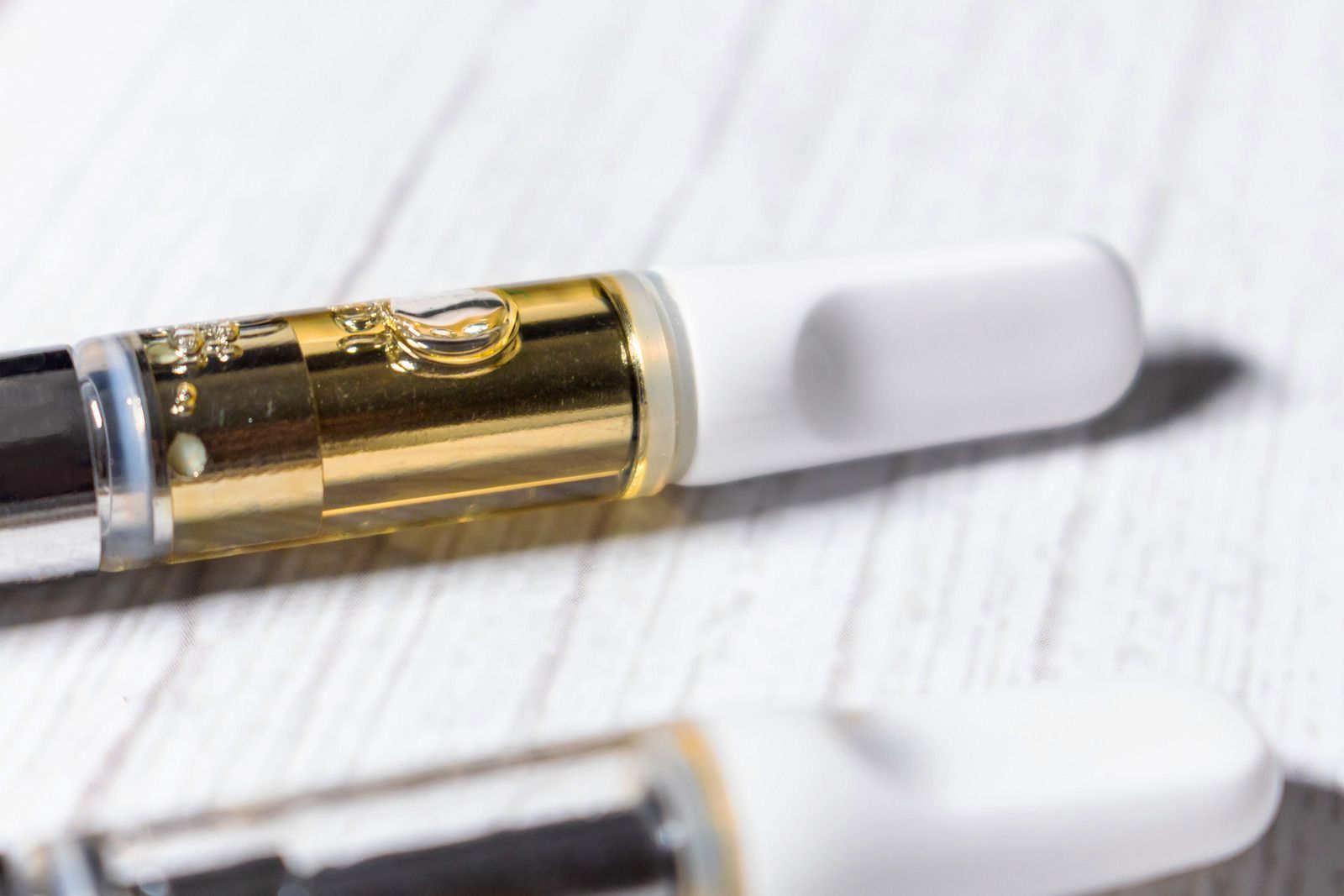 Close-up of two gold and white vape cartridges on a white surface