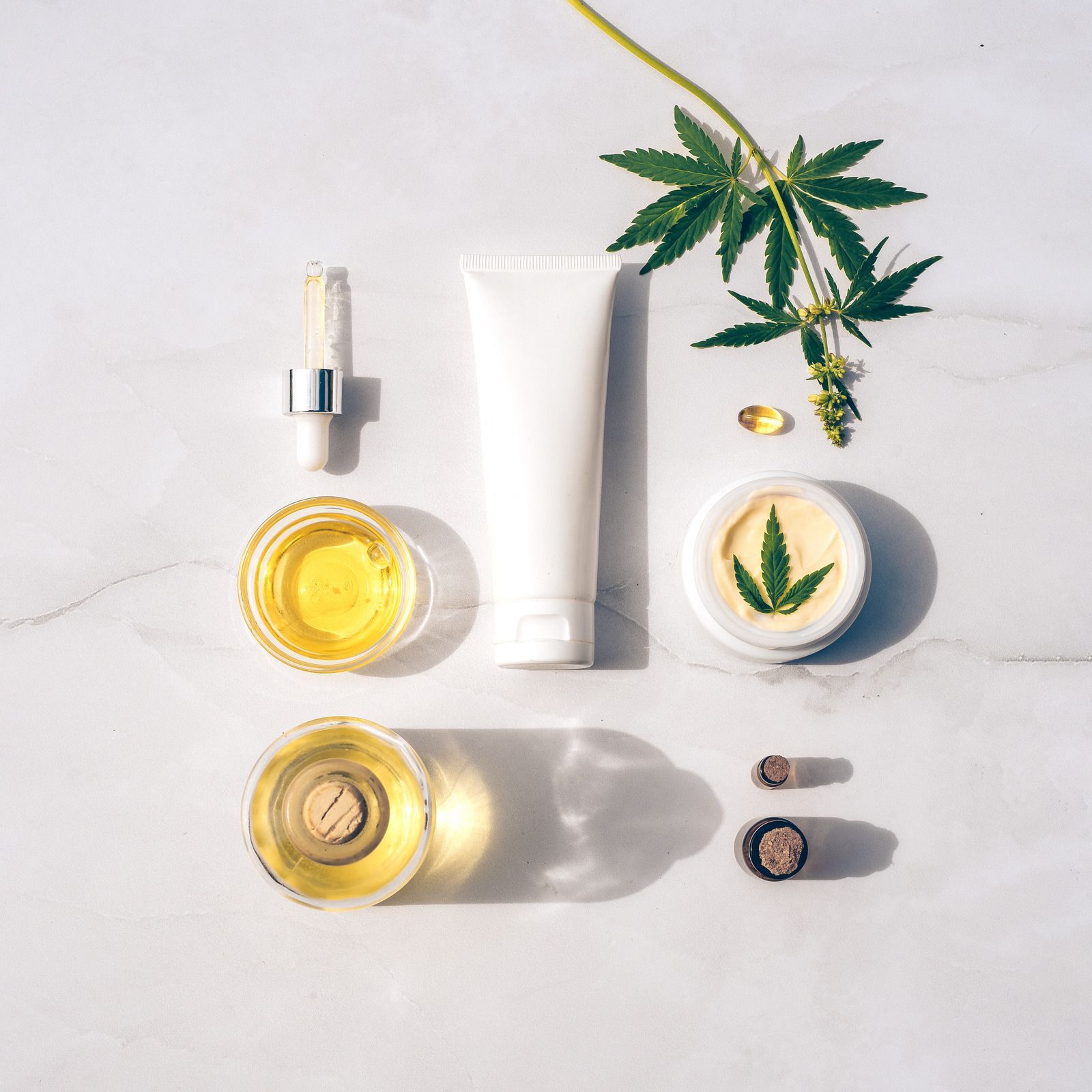 Cannabis skincare products and leaves arranged on a white background.