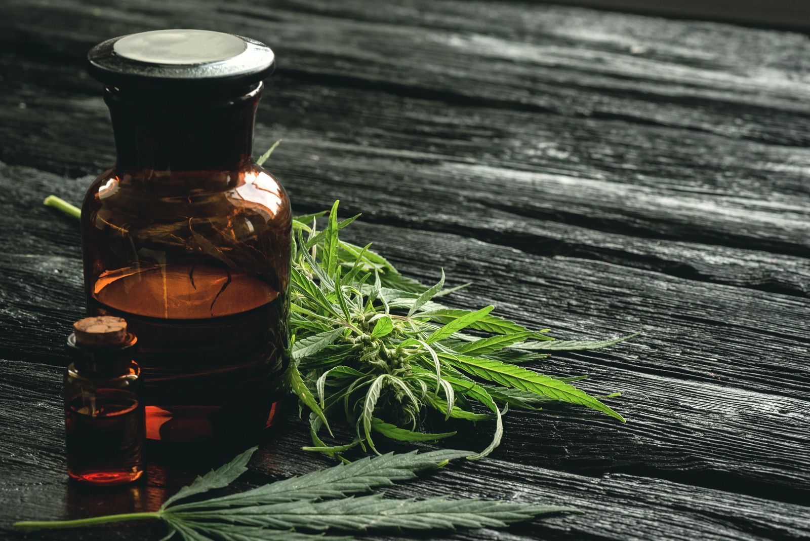 Amber glass bottle and small vial beside fresh green herbs on weathered wood.