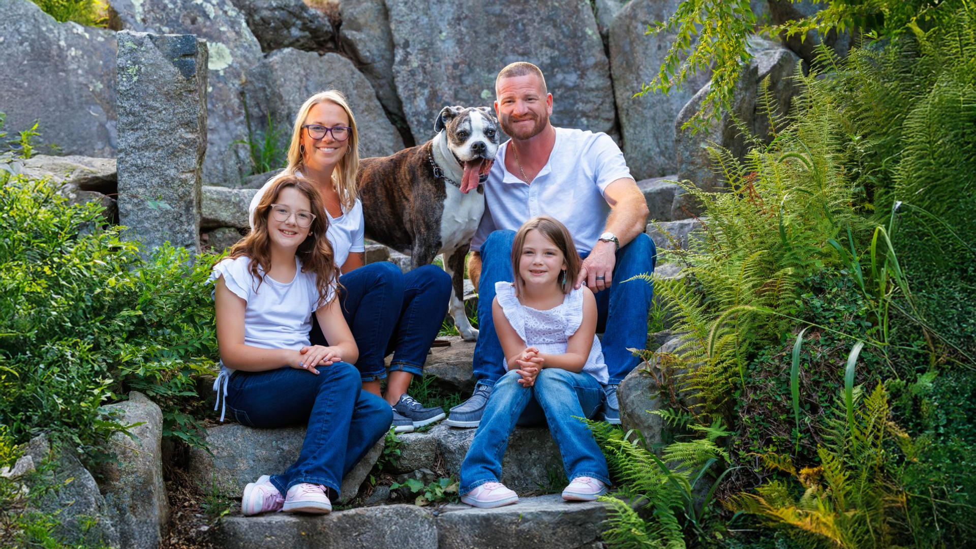 Family sitting on stone steps with their senior dog during an outdoor pet photography session in Massachusetts.