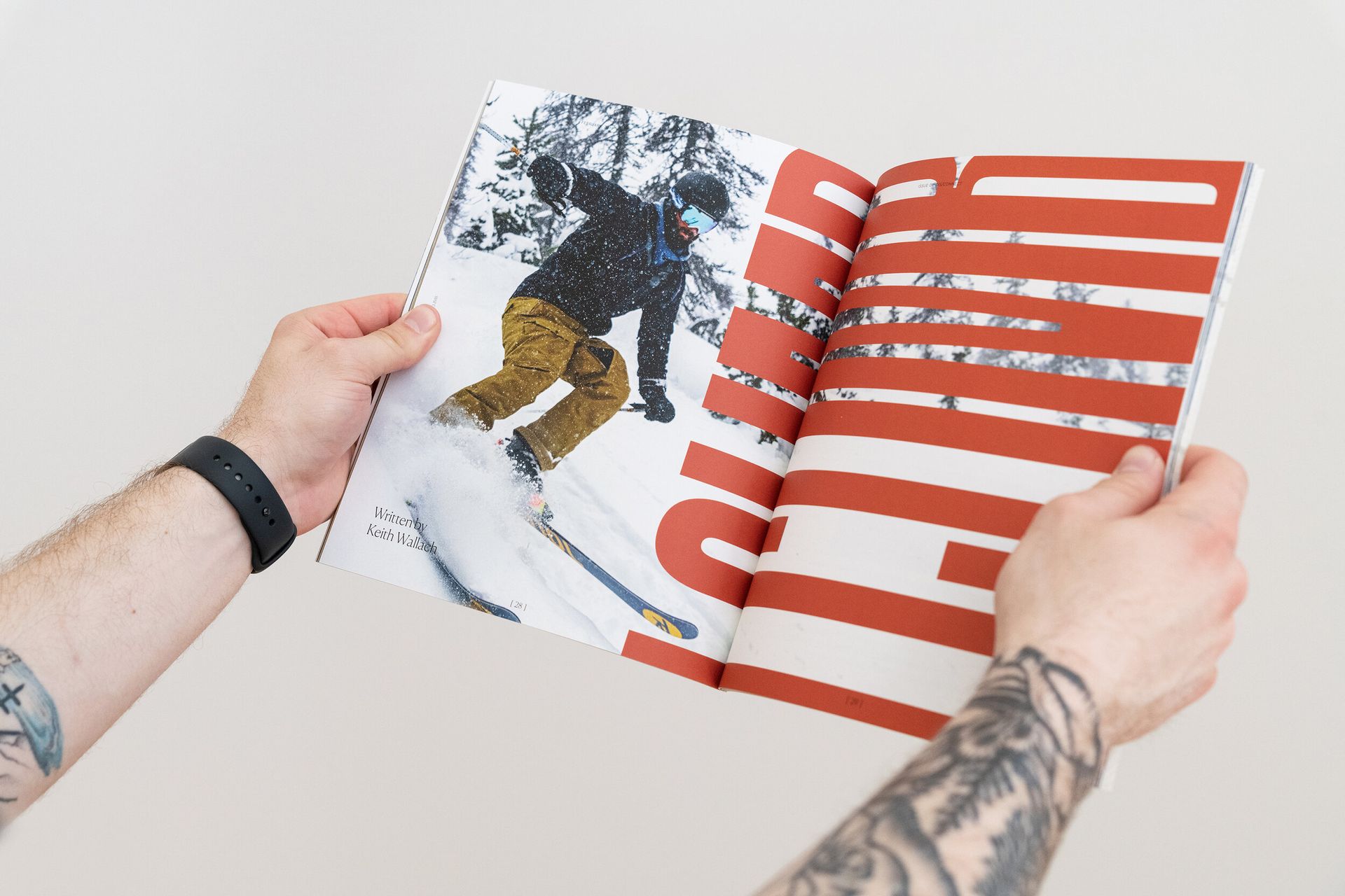 A person with a tattoo on their arm is holding a magazine with a picture of a person skiing on it.