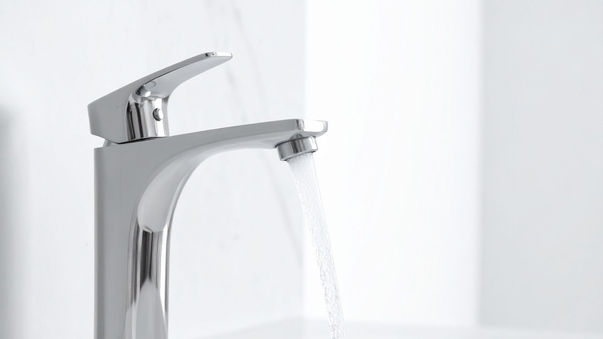 A shiny, modern chrome bathroom faucet with water flowing from the spout against a white background.