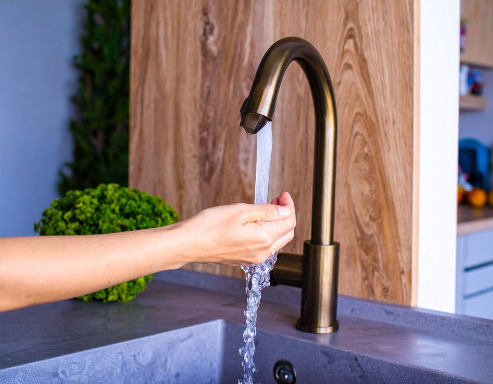 Hand washing under a bronze kitchen faucet with running water