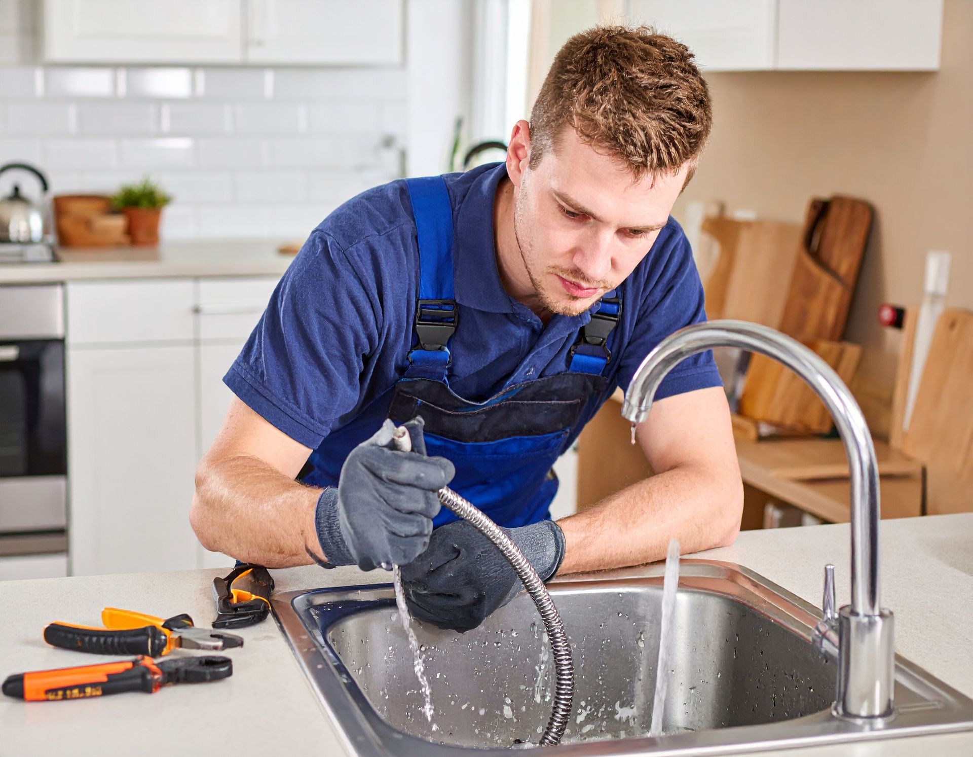 Plumber in blue overalls fixing a sink with water splashing in a kitchen