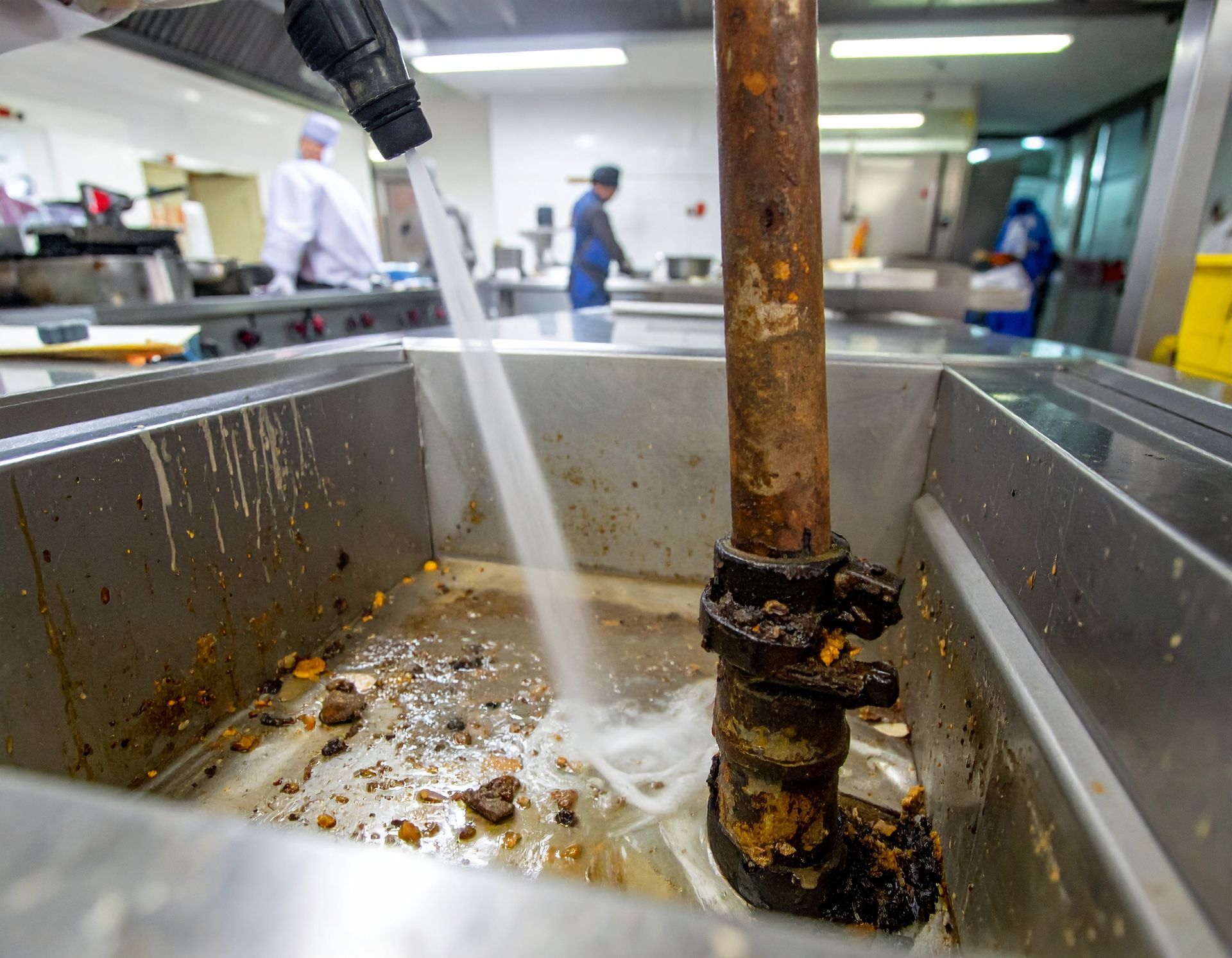 Dirty pipe being sprayed with water in a commercial kitchen sink.
