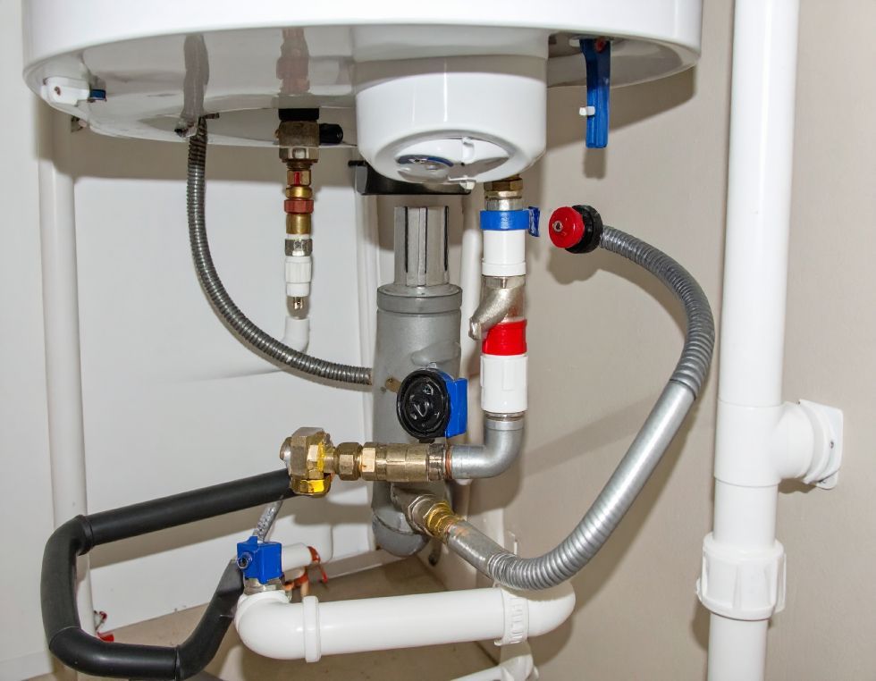Plumbing connections beneath a white tank, featuring pipes, valves, and a flexible hose.