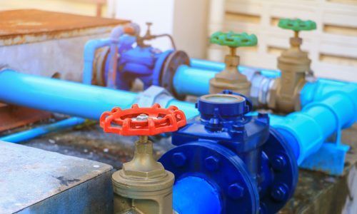 A close-up of blue pipes and industrial valves with red and green handles, installed on a concrete surface.