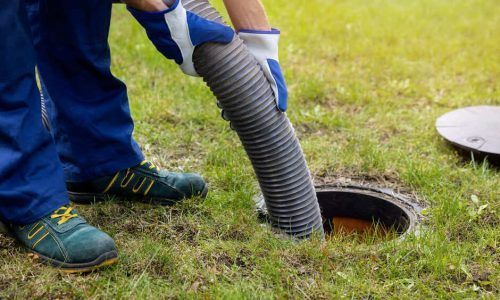 Worker in blue pants and gloves vacuuming a lawn drain with a corrugated hose