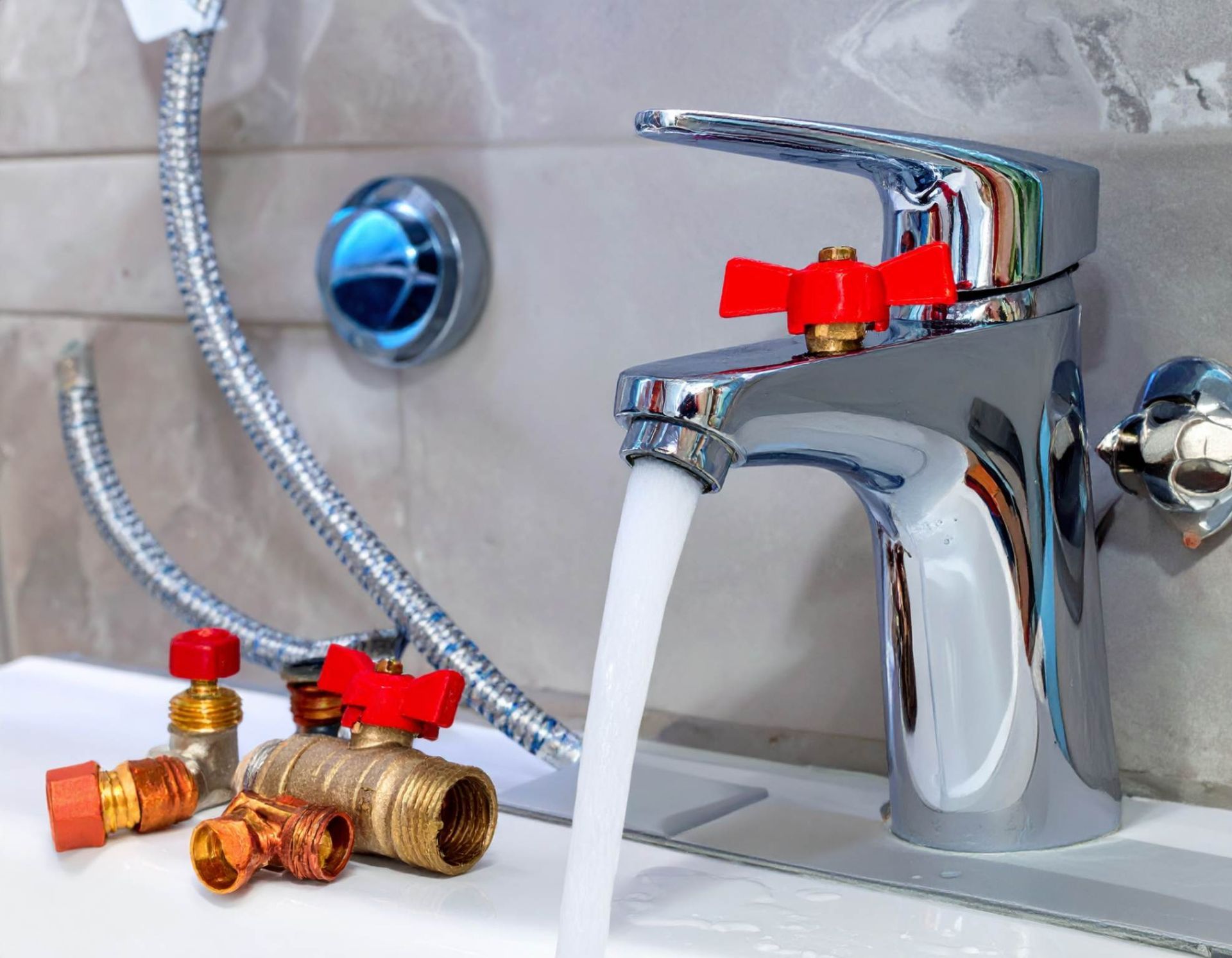 A chrome bathroom faucet flows with water next to plumbing fixtures and fittings on a countertop.