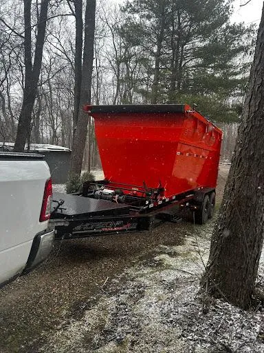 Red dump trailer hitched to a white pickup in a snowy wooded area