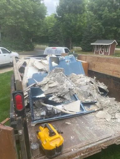 Truck bed filled with broken drywall and debris at a roadside cleanup site.