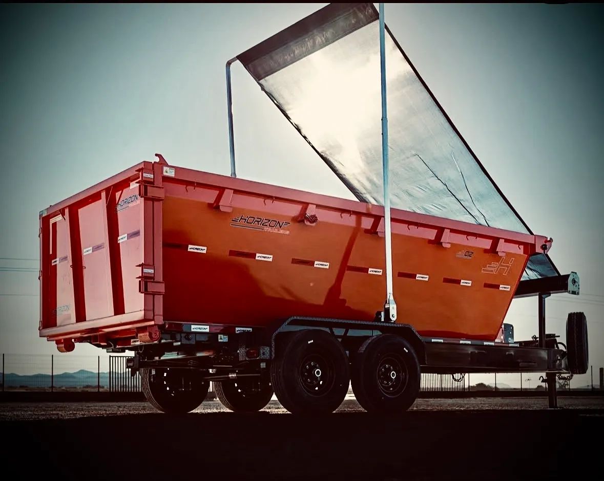 Orange dump trailer with raised tarp on a truck chassis outdoors