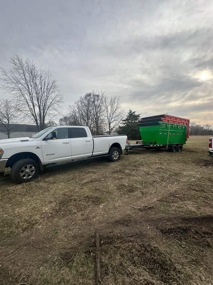 White pickup truck parked beside a green trailer in a muddy field under a cloudy sky.