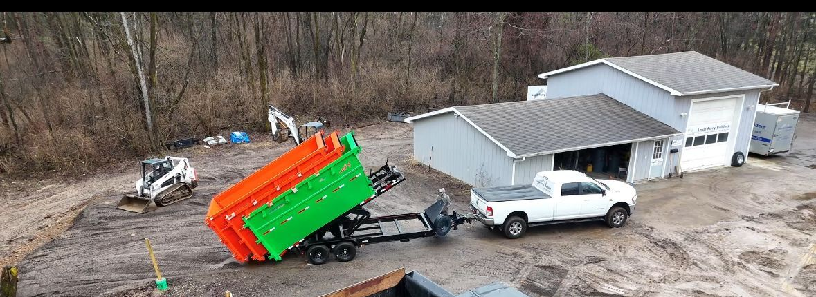 Overturned orange-and-green truck near a white pickup beside a gray building in a gravel lot