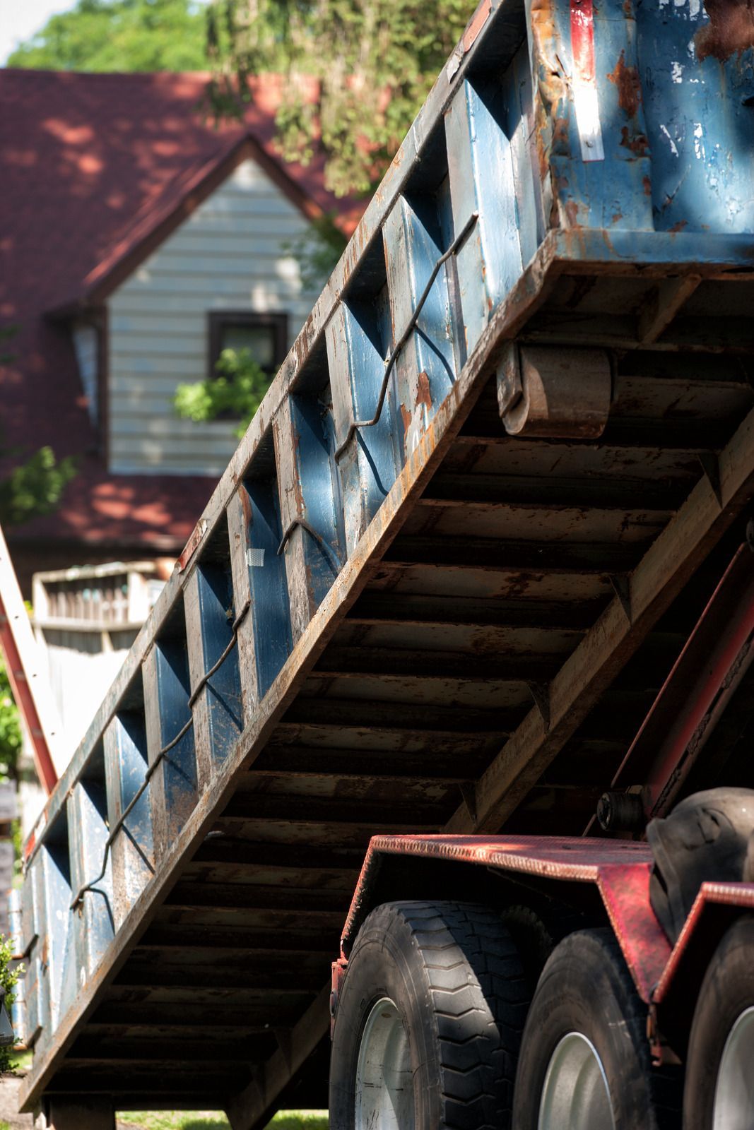 Dump truck bed raised, showing rusty metal and wheels in front of a house.