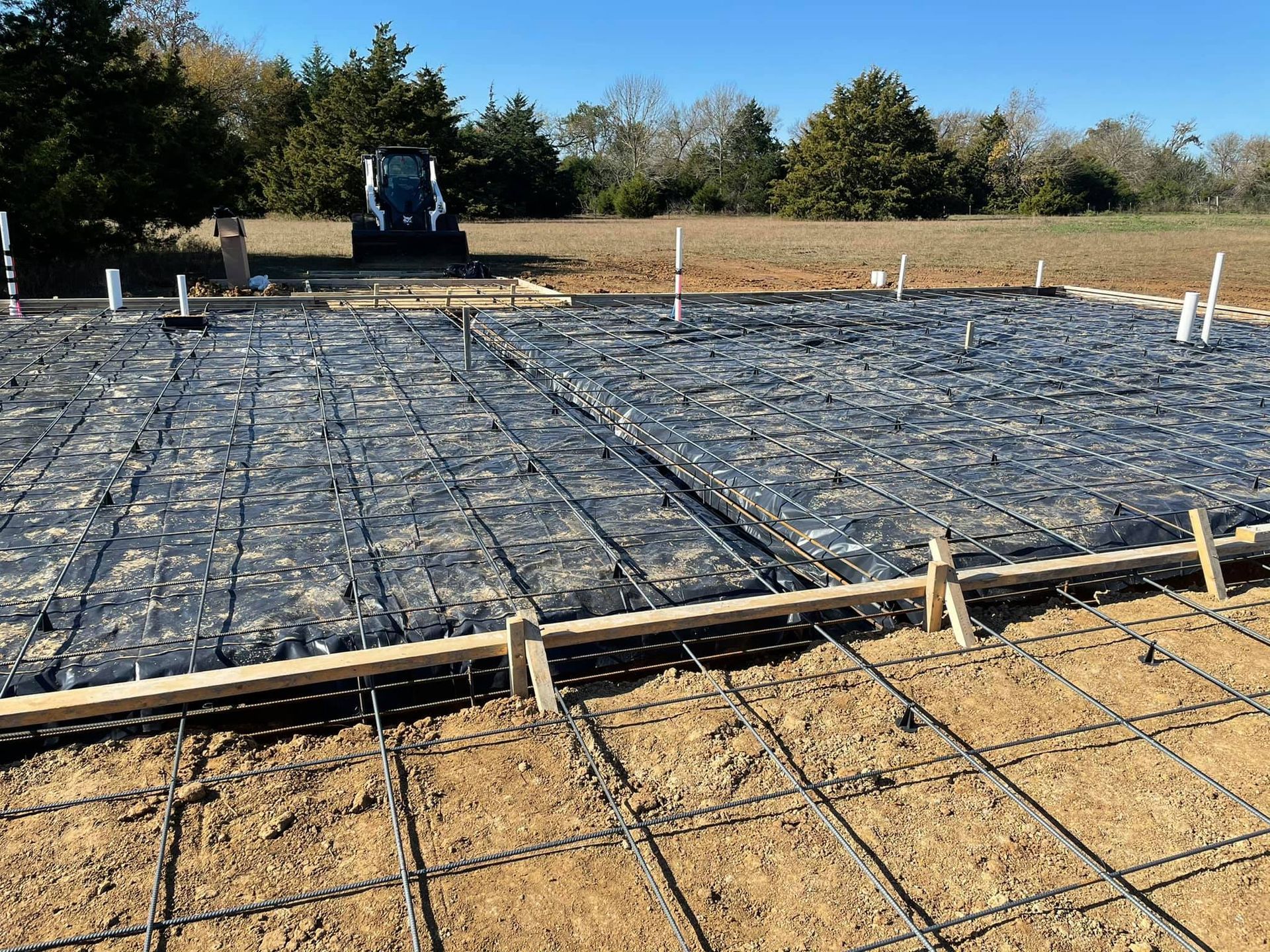 Construction site with rebar mesh over slab formwork and a small excavator in the background