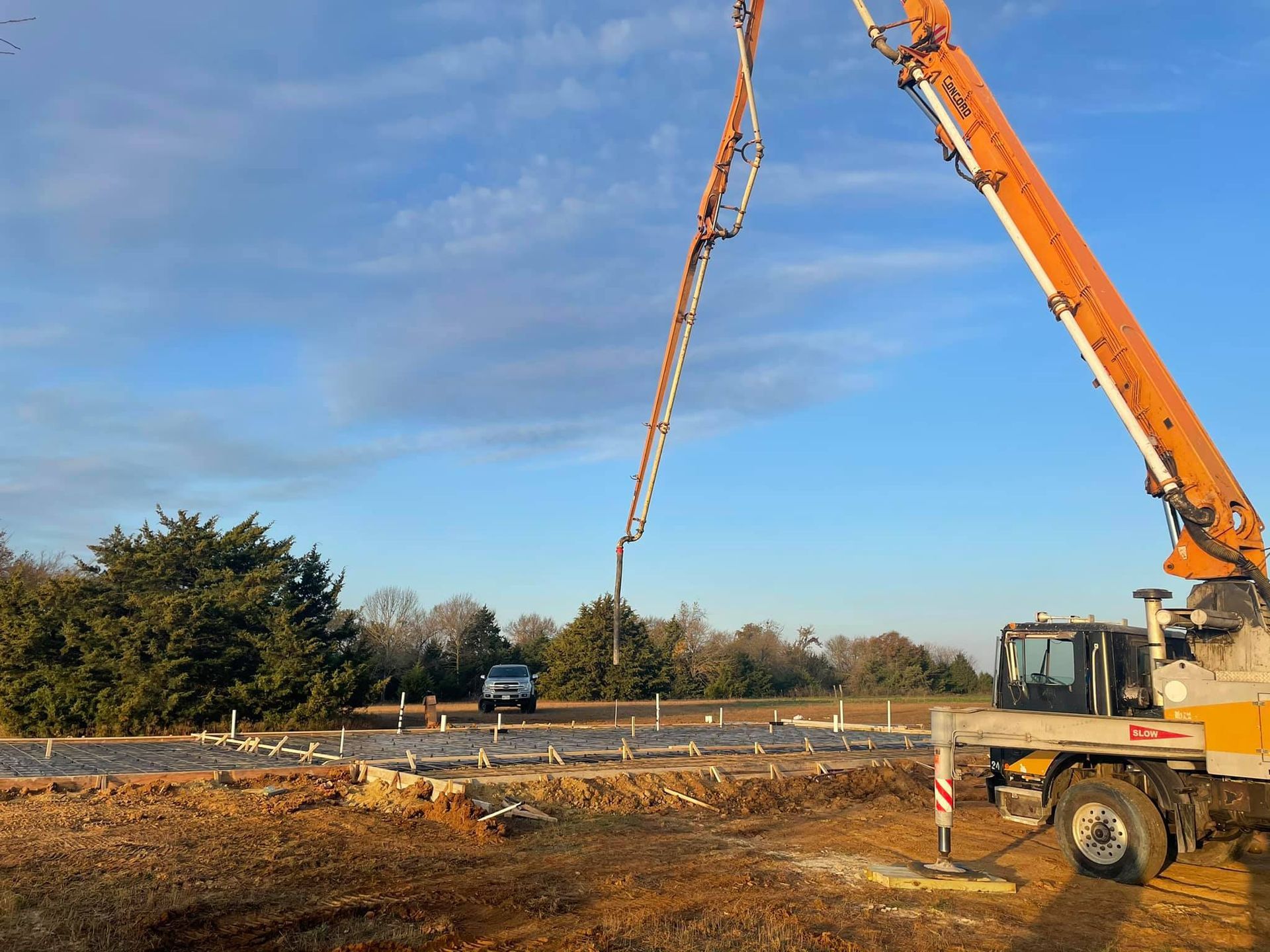 Orange crane lifting a long strap over a roadside construction site under a blue sky