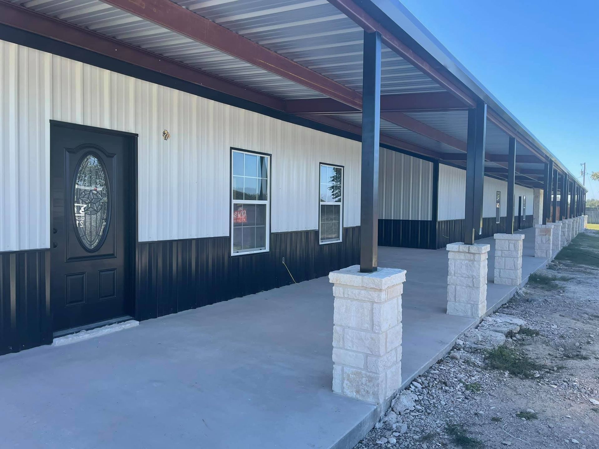 Mobile home porch with black door, white siding, and stone support columns under a red roof