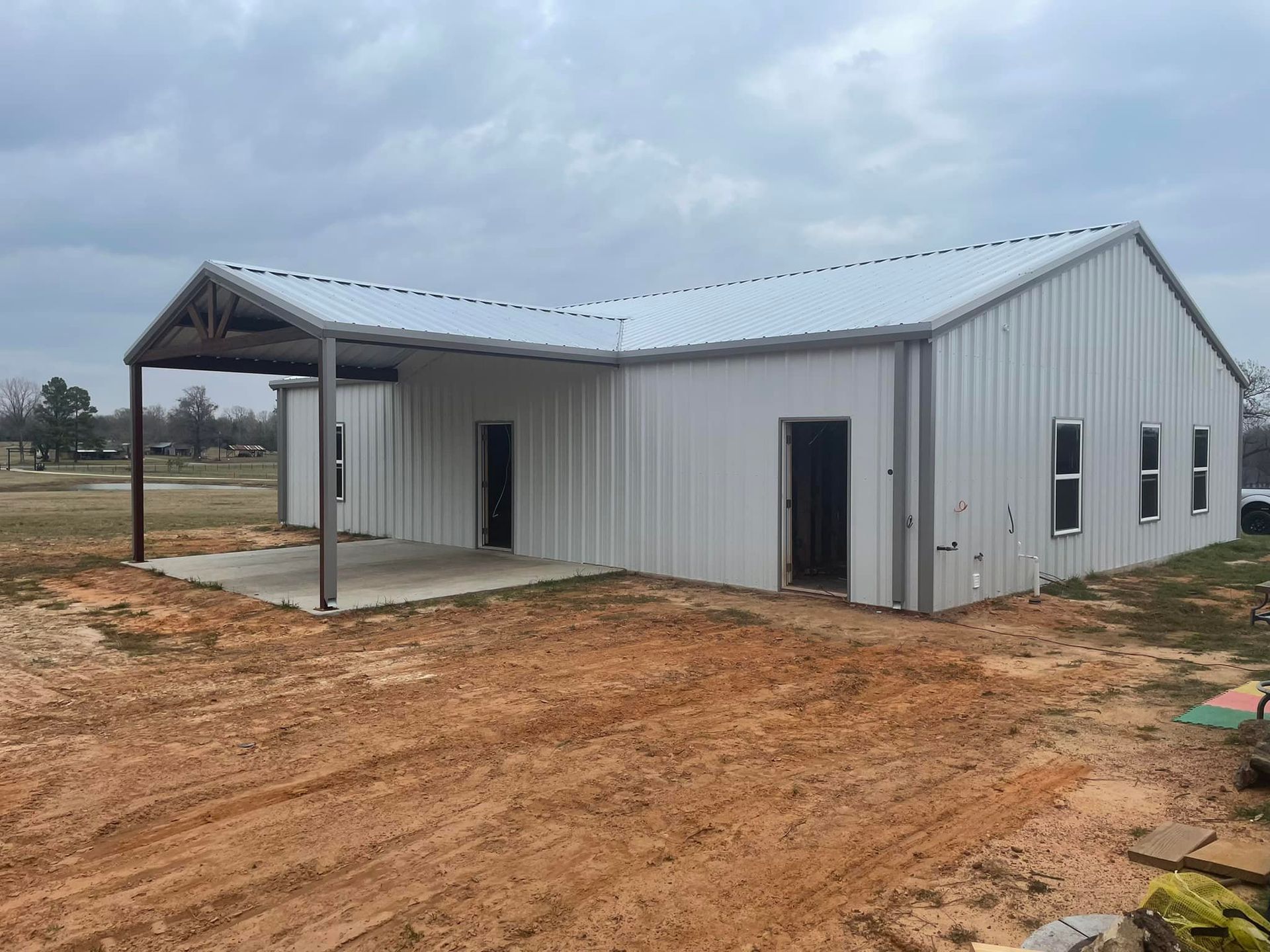 White metal building with a covered porch on a dirt lot under a cloudy sky