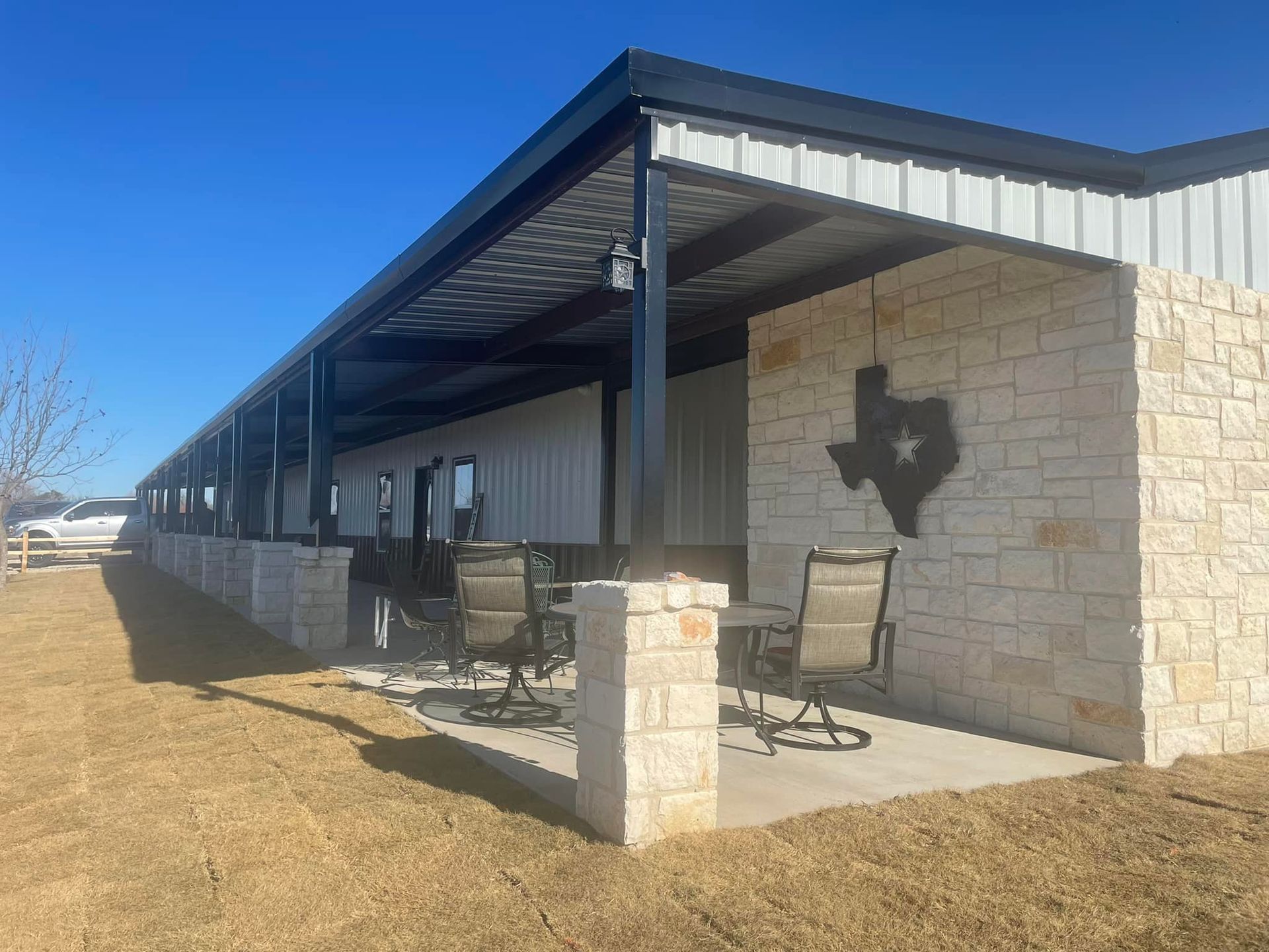 Covered outdoor patio beside a stone building, with tables, chairs, and a Texas-shaped wall decoration.